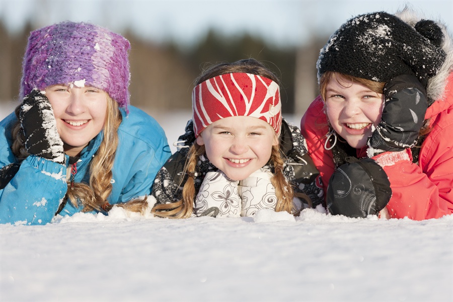 Tre barn i snön ler in mot kameran.