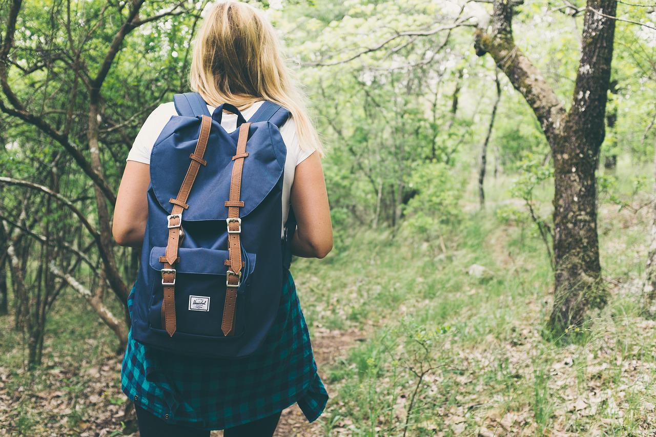 Kvinna med ryggsäck på ryggen, vandrar i skog.