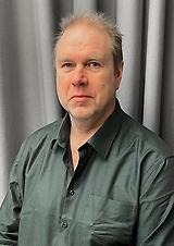 Nils-Erik Flemström, kommunstyrelsens vice ordförande. Porträtt på man i grön skjorta med grå bakgrund.