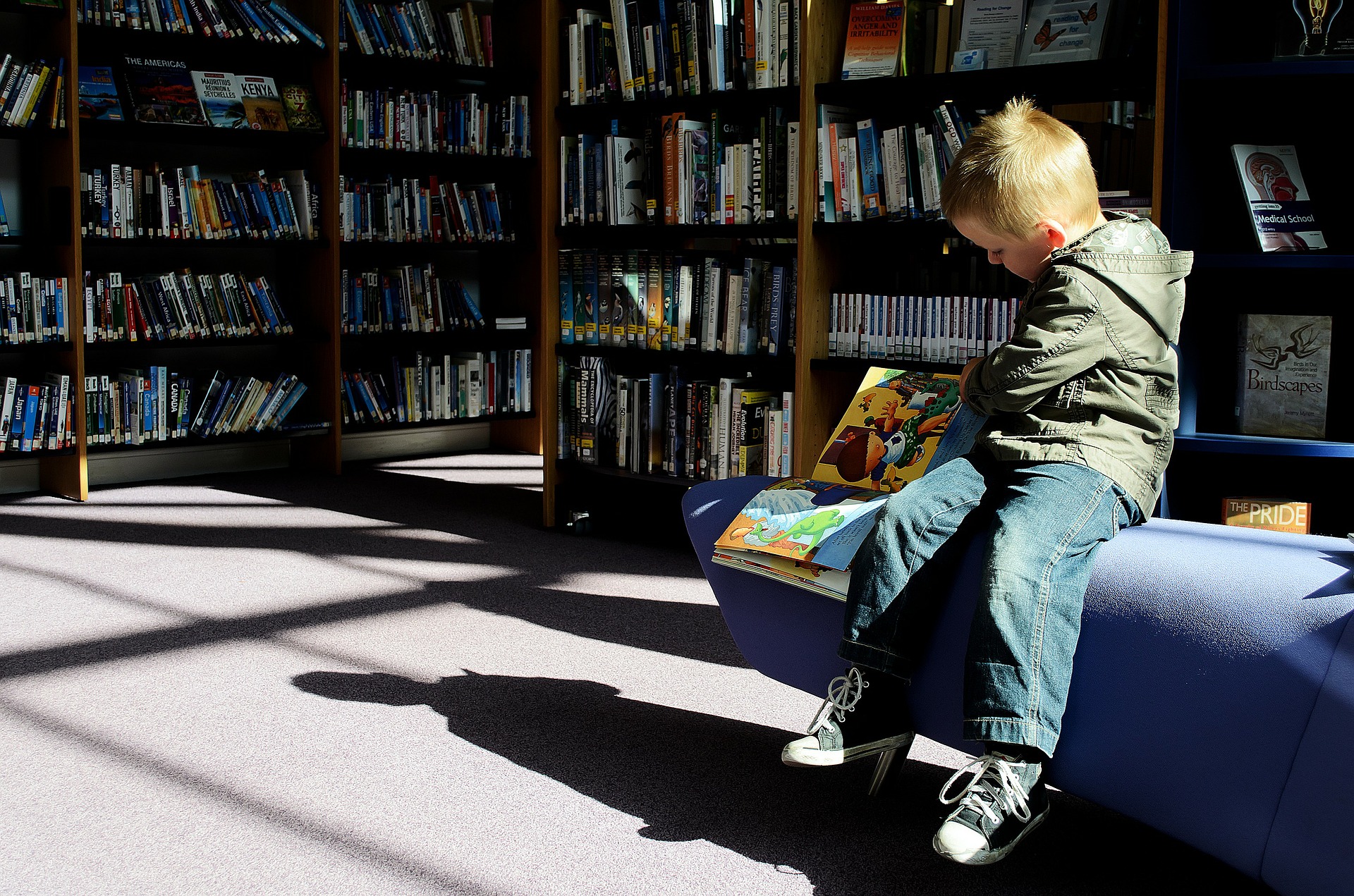 Pojke läser en bok, sitter i bibliotek.