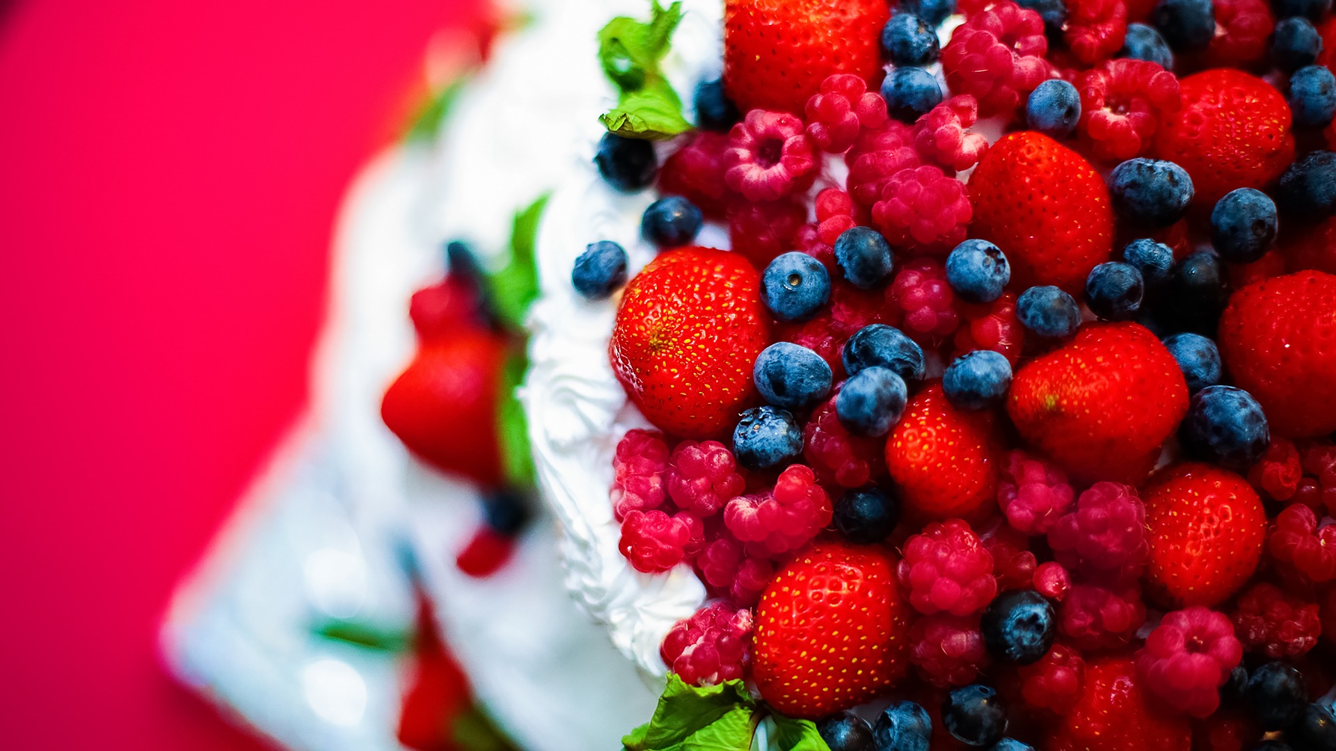 Bilden föreställer en gräddtårta täckt av jordgubbar, hallon och blåbär.