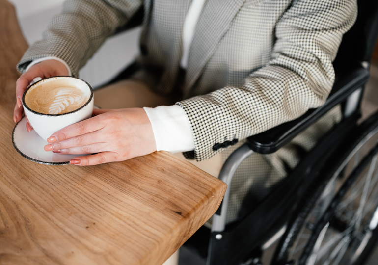 Person i rullstol håller händerna kring en kaffekopp.